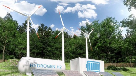 A picture of small wind turbines, solar panels, and hydrogen tanks in a green field, with trees and a blue sky behind.
