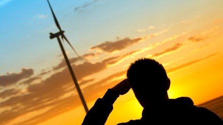 A person standing next to some wind turbines looks out into the sunset.