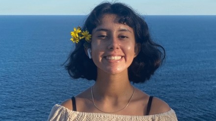 Climate activist Ella Avni, 17, standing looking at the camera and smiling, with the ocean in the background.