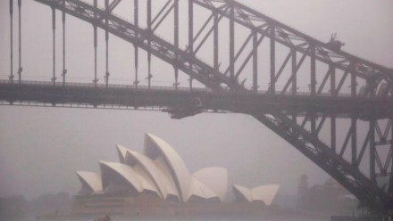 A photograph of the Sydney Opera House in the background, and the Sydney Harbour Bridge in the foreground, on a misty and rainy day.