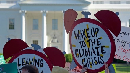 People protesting inaction on climate change holding up signs in front of the White House in Washington - the main sign reads 'wake up to the climate crisis'.