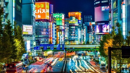 A photograph of a city in Japan at night, with many bright coloured street signs, and the blur of car headlights on the highway.
