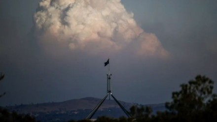 A photograph of Australia&#039;s Parliament House with a huge plume of bushfire smoke rising in the distance.