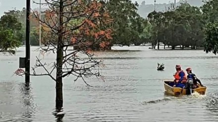 SES crew members in a small boat, sailing through flood waters in a suburban area.