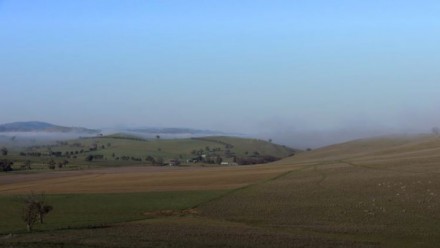 A photograph of green rolling hills, with a slight mist above them. 
