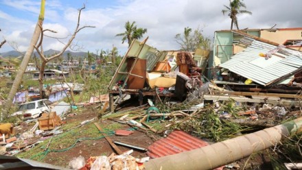 A photograph of the aftermath of a cyclone, with a damaged house to the right.