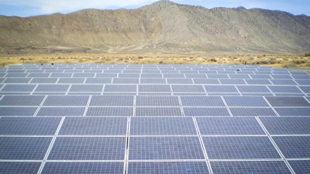 An image of a solar farm, with a hill in the background and a blue sky. 