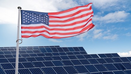 American flag flutters on the backgorund of solar panels.