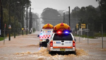 Two SES vehicles with dinghies on their roofs travel down a flooded road