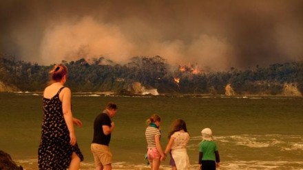 Evacuees on a beach look on as bushfire burns through the NSW south coast township of Malua Bay.