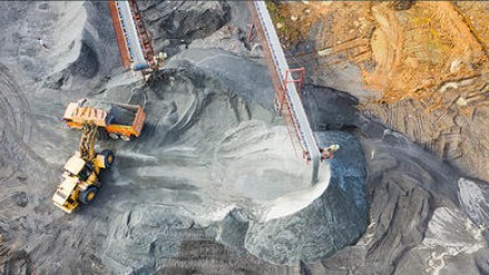 An aerial view of a tractor moving coal into the back of a truck in an open cut mine.