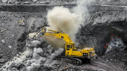 A yellow tractor shovels coal in an open cut mine.