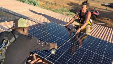 Photo of two people installing a solar panel on a roof top in the Norther Territory