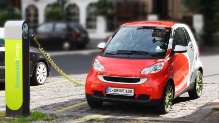 A red electric car plugged into a lime green charging station.