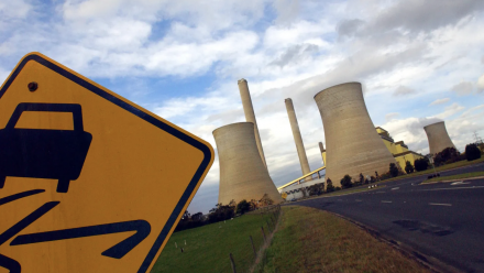 A 'windy road' road sign, with a coal-fired power station in the background.