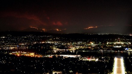 An image looking over Canberra at night time on 31 Jan 2020, with the hills in the background lit up orange with the Orroral Valley fire burning.
