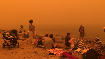 Isobel Davis' family on the beach at Batehaven, shrouded in orange bushfire haze, after having lost her parents' house to the bushfires.