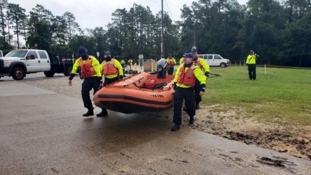 A photograph of a team of rescue workers in high-vis clothing carrying an inflatable boat.
