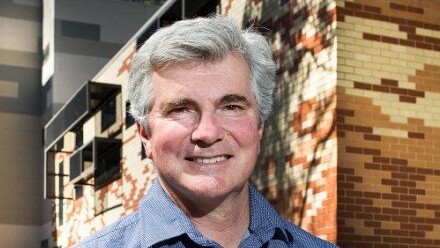 A photograph of Prof Mark Howden standing outside the Frank Fenner building at The Australian National University, smiling and looking at the camera.
