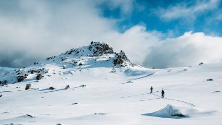 Two men walk up to the top of a snow-capped mountain.