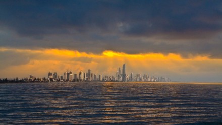 An image of the Gold Coast from the ocean and during a dust storm, with a heavily overcast sky, but rich orangey-golden sunlight streaming through a break in the clouds.