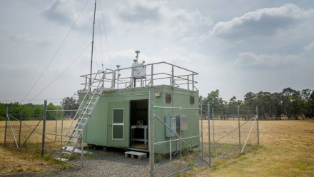 A light green air monitoring station in Canberra, sitting in the middle of a field of dry grass.