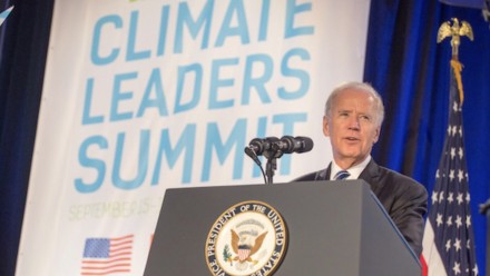 A photograph of Joe Biden delivering a speech from a lectern with the US Presidential Seal on it, and a sign behind reading Climate Leaders Summit.