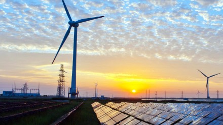 The sun setting behind wind turbines and a field of solar panels.
