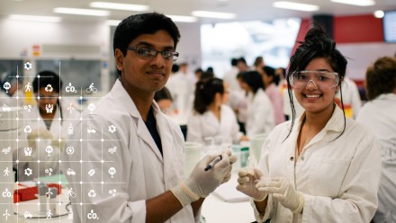 Two students wearing protective glasses and white lab coats smiling at the camera.