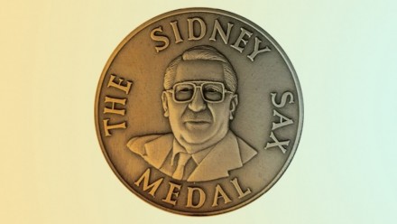 A photograph of the Sidney Sax medallion, with the words &#039;The Sidney Sax Medal&#039; around the outside, and an engraving of Sidney Sax in the middle.