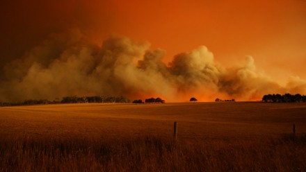  A fire at Churchill, Victoria on Black Saturday 2009. The sky is a dark orange colour, with a thick plume of smoke rising in the distance from where the fire is burning.