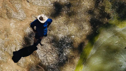 A man stands beside a drying-out river.