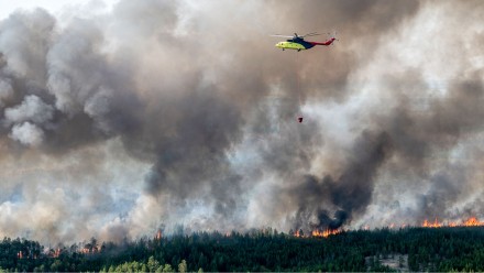 A photograph of a helicopter dropping water on a wildfire in Siberia