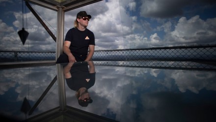 Nick Dutton, fire tower operator, Rural Fire Service in the Kowen Forest fire tower near Canberra. Nick is wearing a cap and sunglasses, and looking to the right. The sky behind him is cloudy.