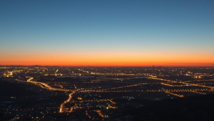 A photograph of a sunset over a city-scape, with the city lights shining beneath a blue-to-orange sky.