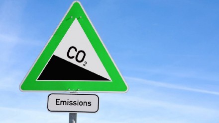 An image of a triangle road sign, with CO2 written on it on a downwards slope, and &#039;emissions&#039; written beneath it.