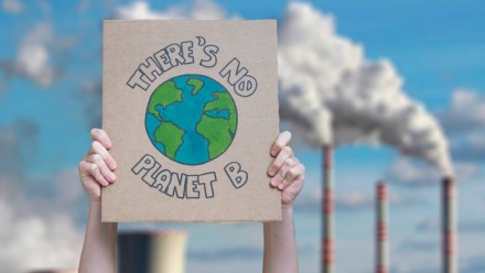 Someone holding up a sign in front of a coal-fired power station that says &#039;there is no planet B&#039;