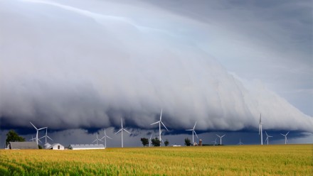 A photograph of storm clouds rolling in over a field of wind turbines.