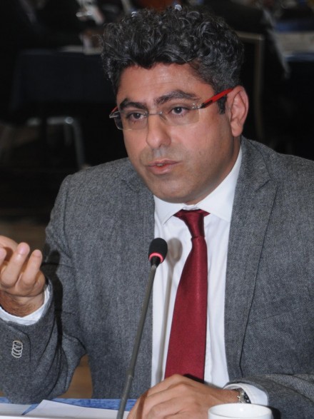 A photograph of Dr Saleh, sitting at a table with a microphone in front of him, speaking.