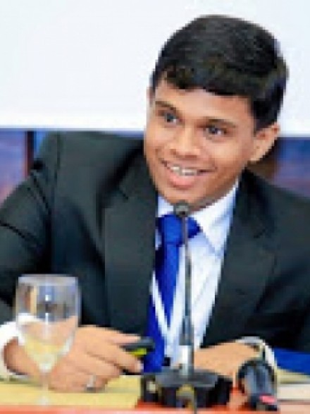 A photograph of Roshen Fernando, sitting at a desk behind a microphone, leaning forwards to speak into it.