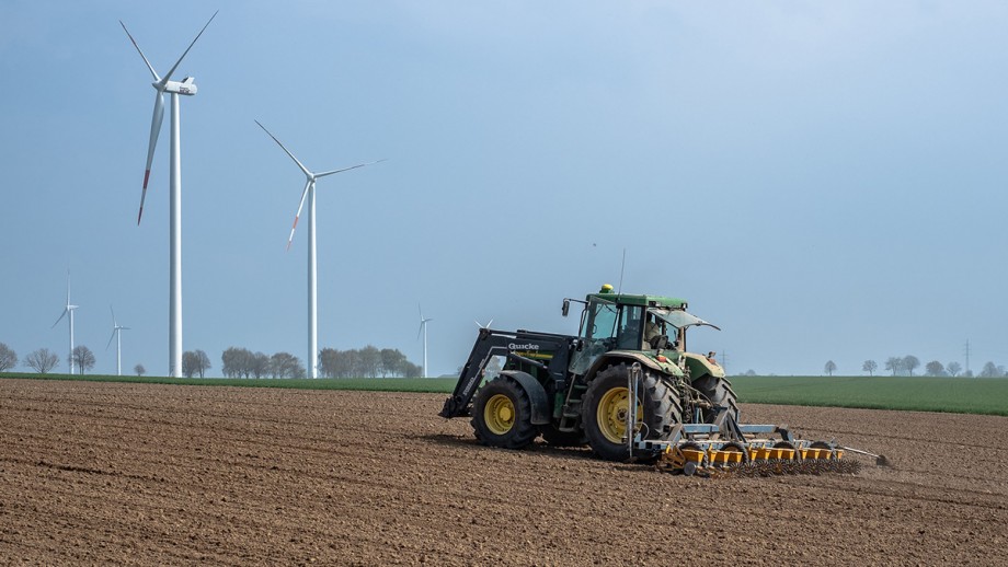 A tractor on a crop with wind turbines in background