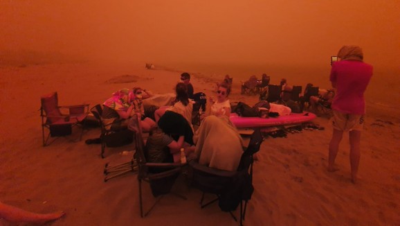 People evacuating from bushfires in a red haze at Batemans Bay beach on New Year's Eve, 2019