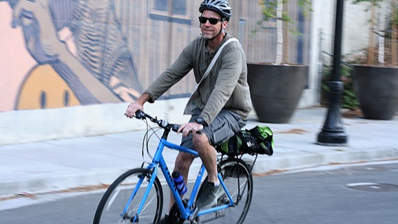 A man wearing sunglasses and helmet riding a bike in a street